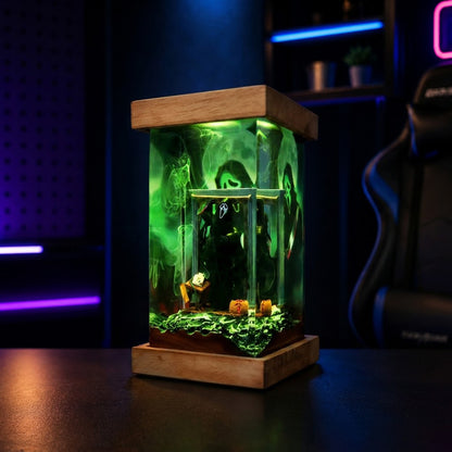 A small glass aquarium with a wooden top and base, illuminated in glowing green, sitting on a dark tabletop in a dimly lit room with blue ambient lighting.